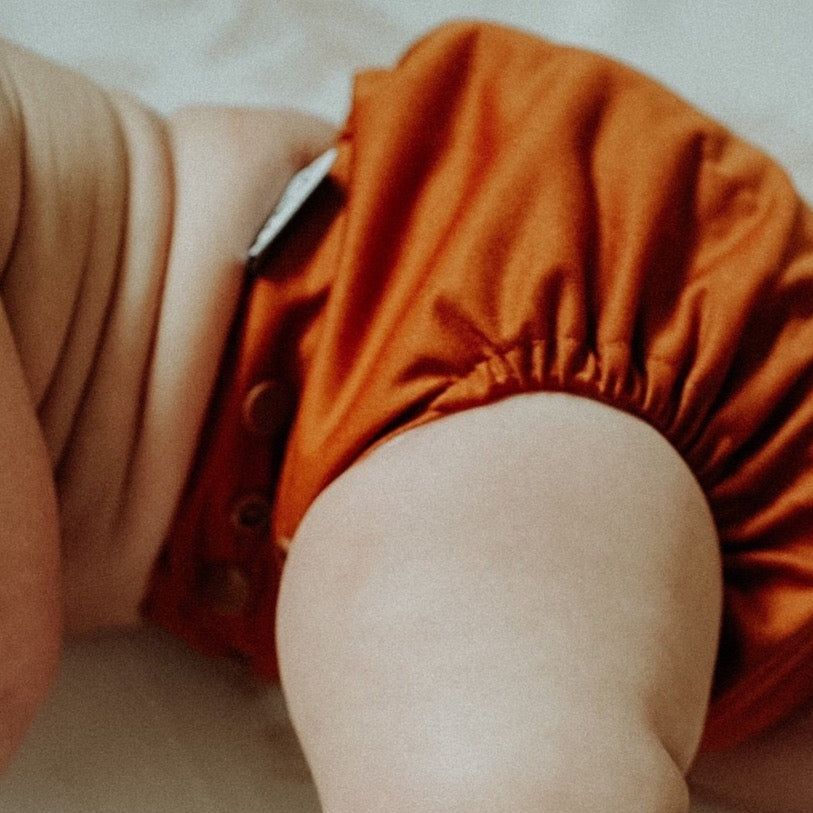 A cute baby wearing their brown reusable nappy from Frank Nappies